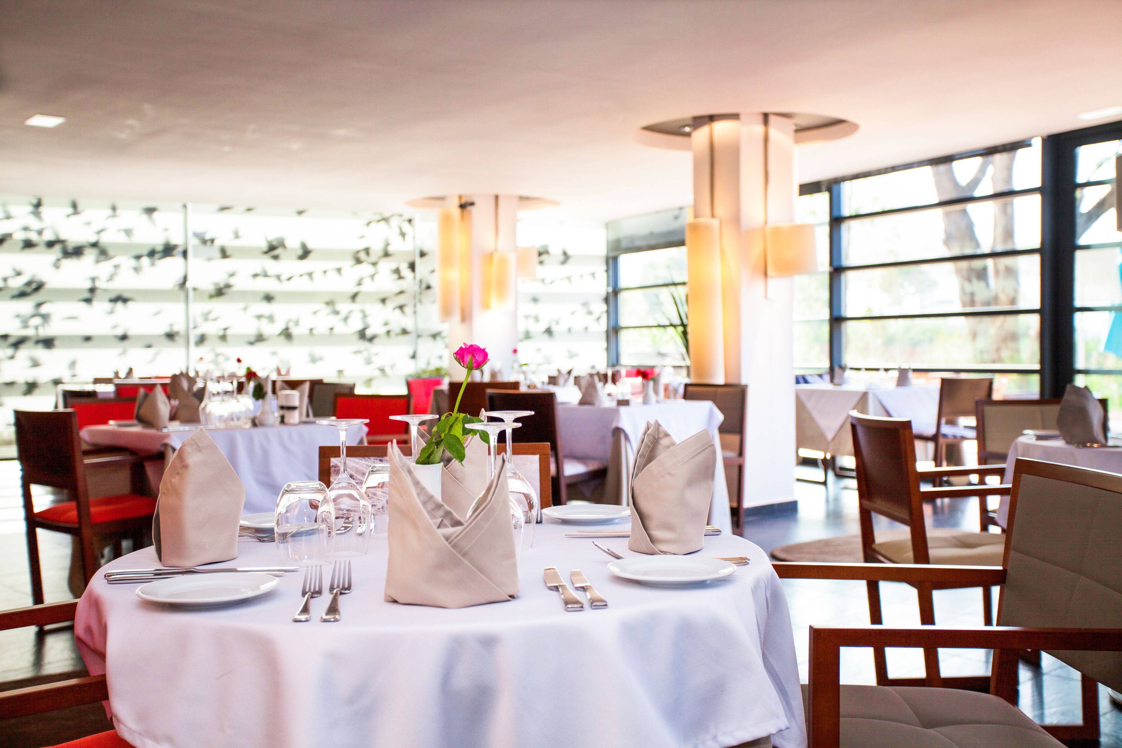 A restaurant with round tables set for dining, featuring white tablecloths and beige napkins.