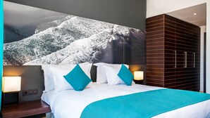 A modern hotel room with a large bed, two nightstands, a wall-mounted TV, and a dark wooden wardrobe. - Hotel Souani (Ait Youssef Ou Ali)