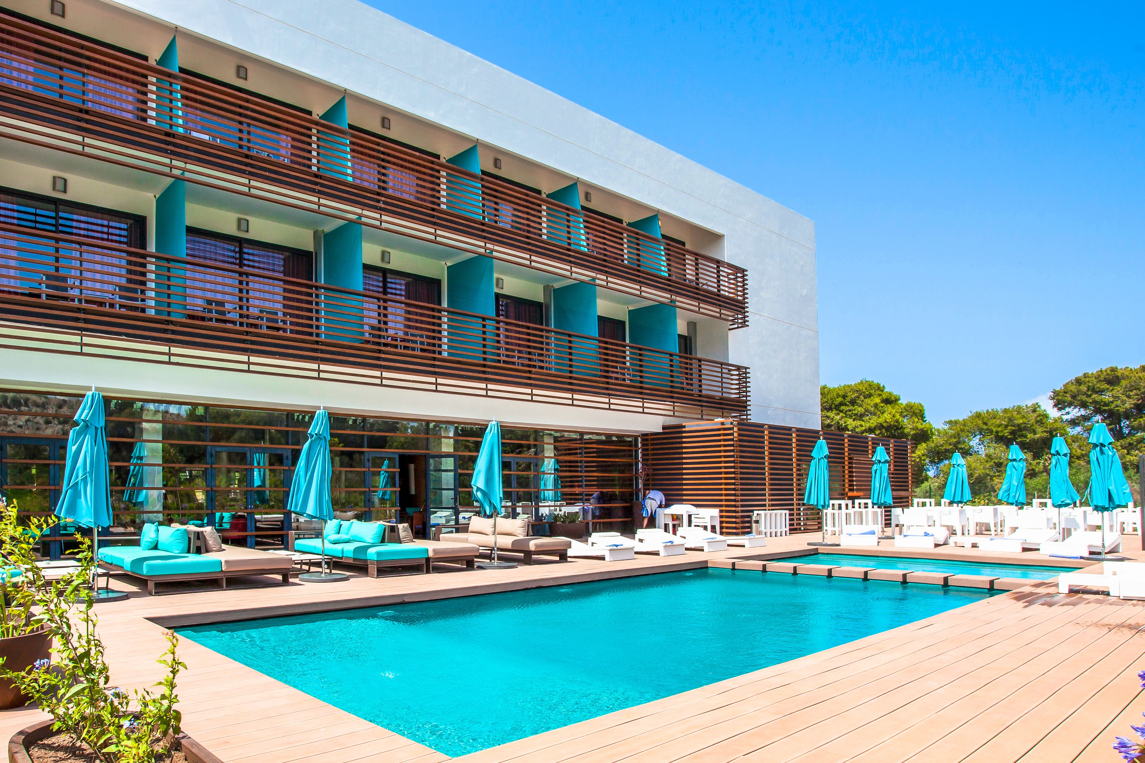 Un hotel moderno con una piscina grande, zona de estar exterior y varios balcones.