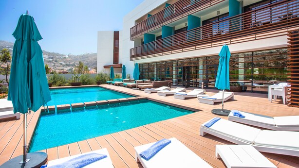 A modern outdoor pool area with lounge chairs and umbrellas, a wooden deck, and a building with balconies. - Hotel Souani (Ait Youssef Ou Ali)