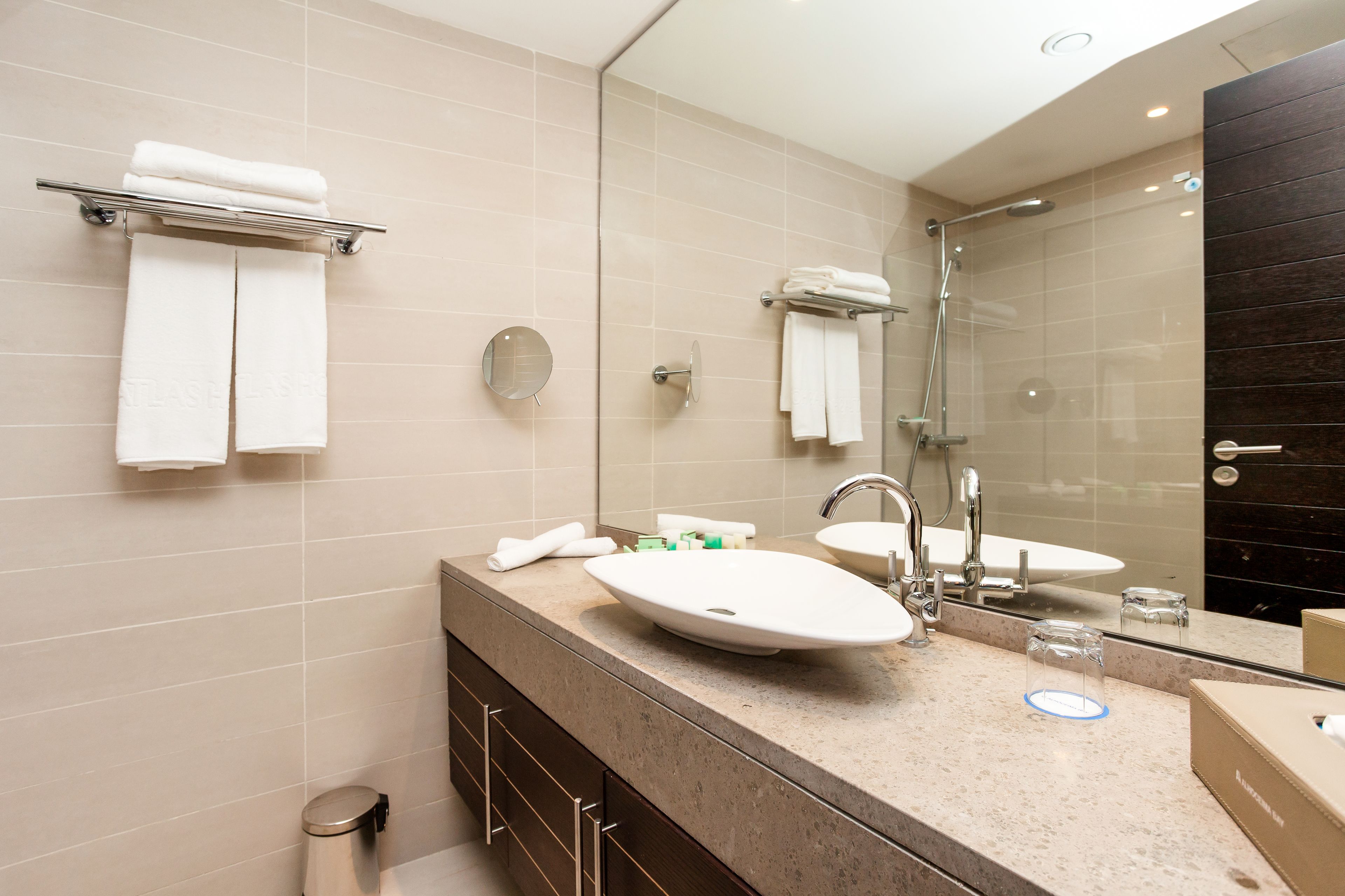 A modern bathroom with a large mirror, two sinks, a shower, and a towel rack.