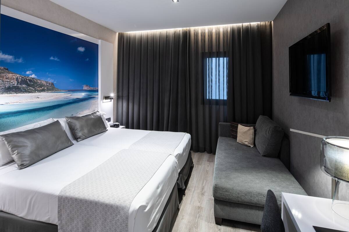 Ein modernes Hotelzimmer mit einem großen Bett, einer Sitzecke, einem Fernseher und Blick auf einen Strand.