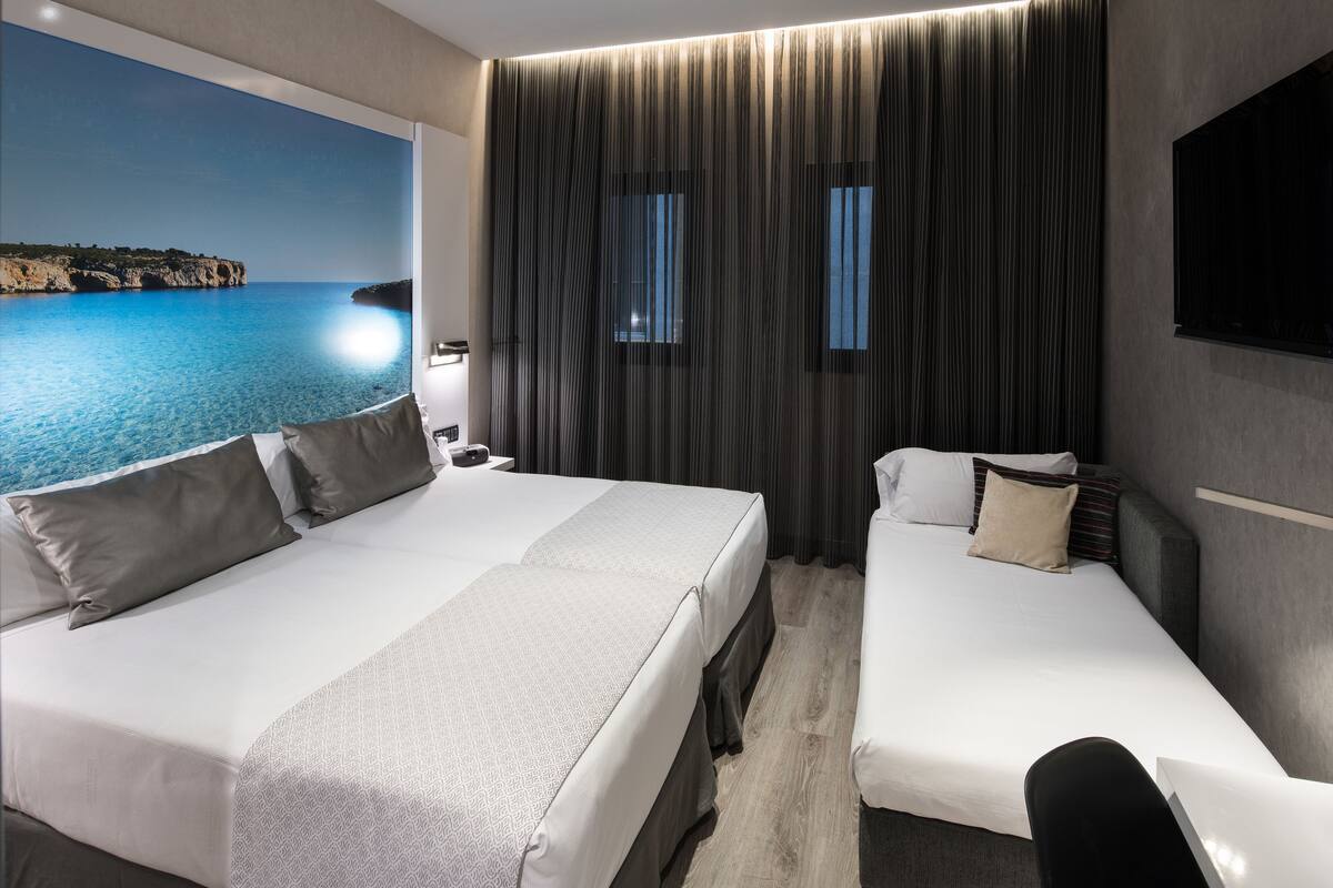 Ein Hotelzimmer mit zwei Betten, einem großen Fenster mit Meerblick und einem an der Wand befestigten Flachbildfernseher.