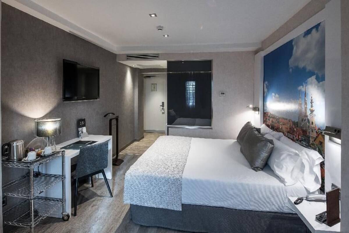 Ein modernes Hotelzimmer mit einem Bett, einem Schreibtisch mit Stuhl, einem an der Wand befestigten Fernseher und einem großen Fenster.