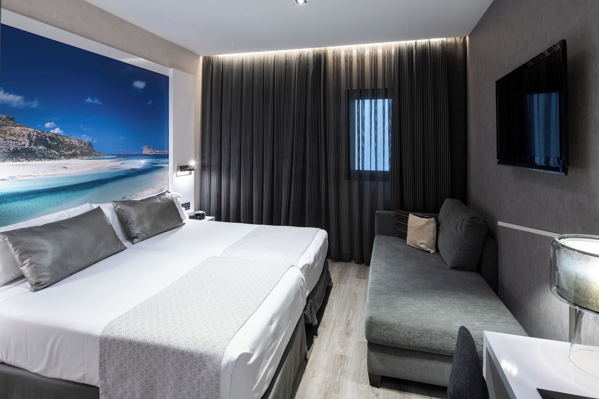 Ein modernes Hotelzimmer mit einem großen Bett, einer Couch, einem Fernseher und Blick auf einen Strand.
