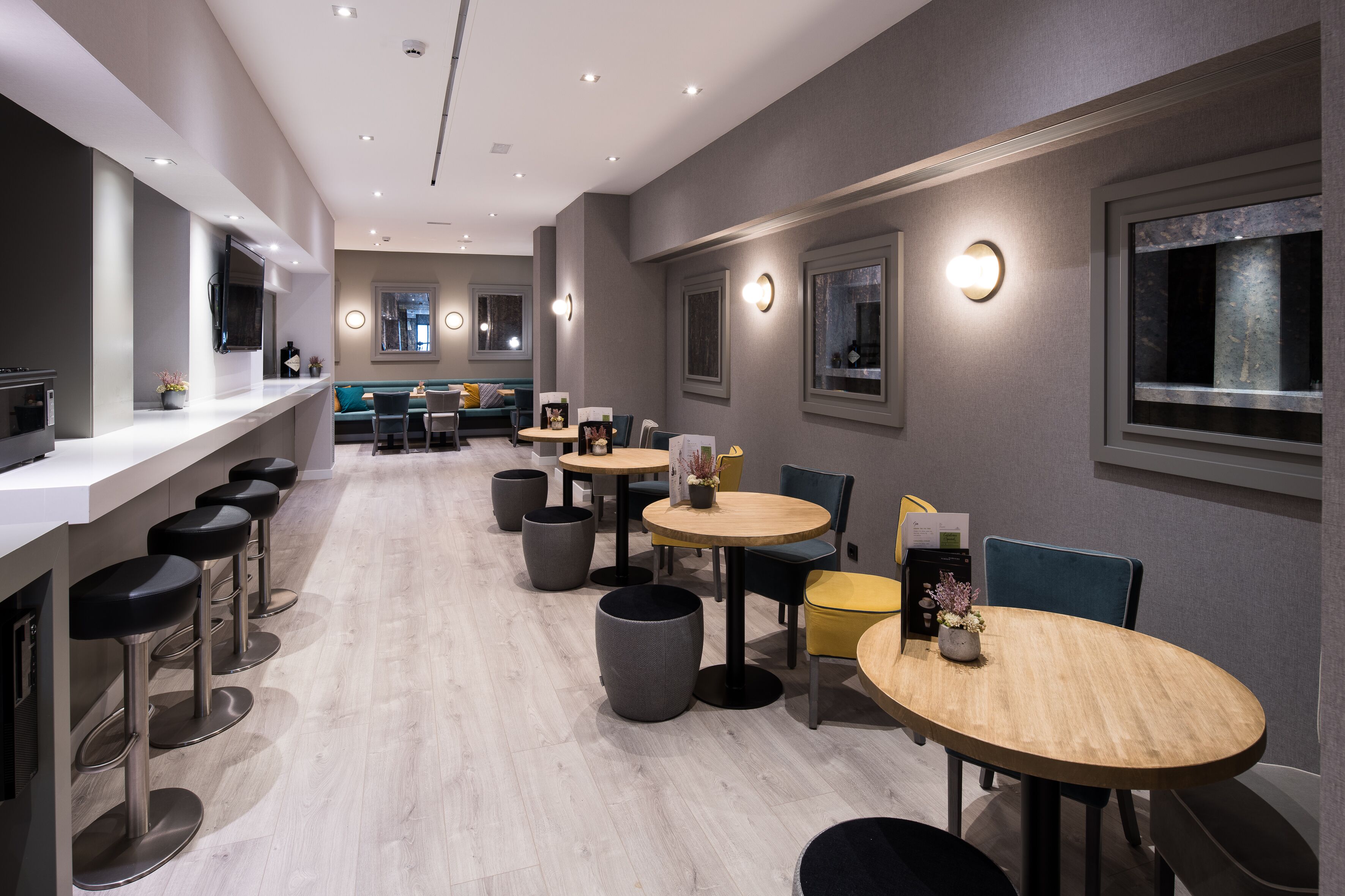 Ein modernes Restaurant mit einer langen Theke, mehreren Sitzhocker, runden Tischen und einer gemütlichen Sitzecke mit einer Couch und Sesseln.