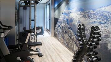 Una palestra con attrezzature per l'esercizio fisico, un tapis roulant e un murale raffigurante un paesaggio montano.