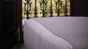 A balcony with a wrought iron railing, a bed with a patterned bedspread, and a view of buildings with green shutters in the background. - Catalonia Gran Vía BCN (Barcelona)