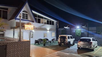 A hotel with a sign reading "Hotel Express Inn," a parking area with two cars, and a building with a tiled roof and a balcony.