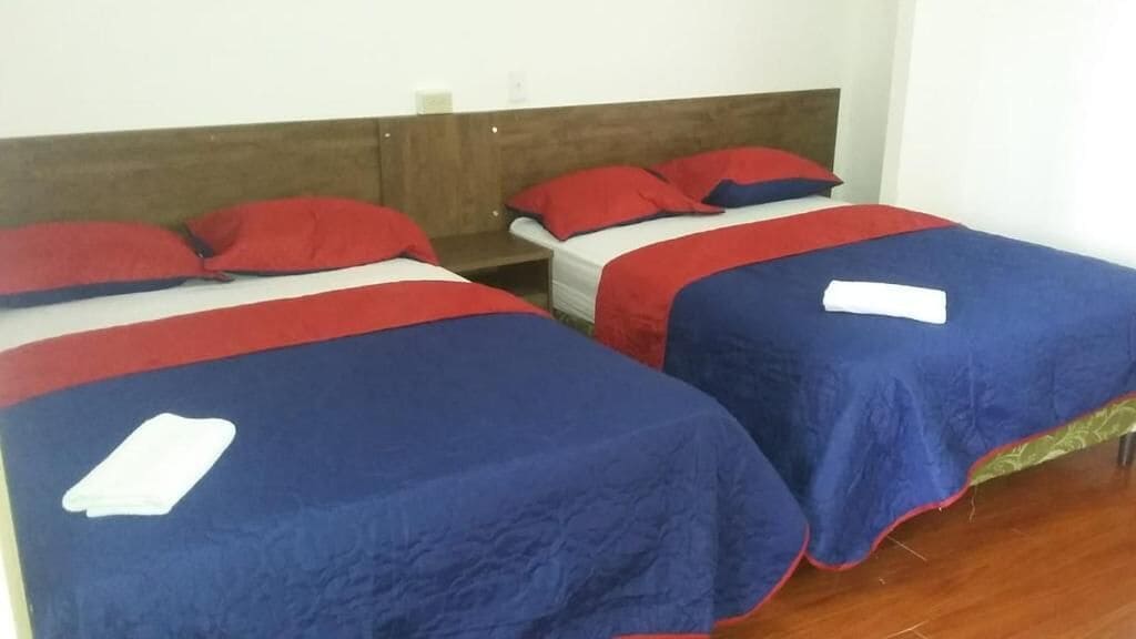 Two single beds with red and blue bedding, wooden headboards, and a white wall.