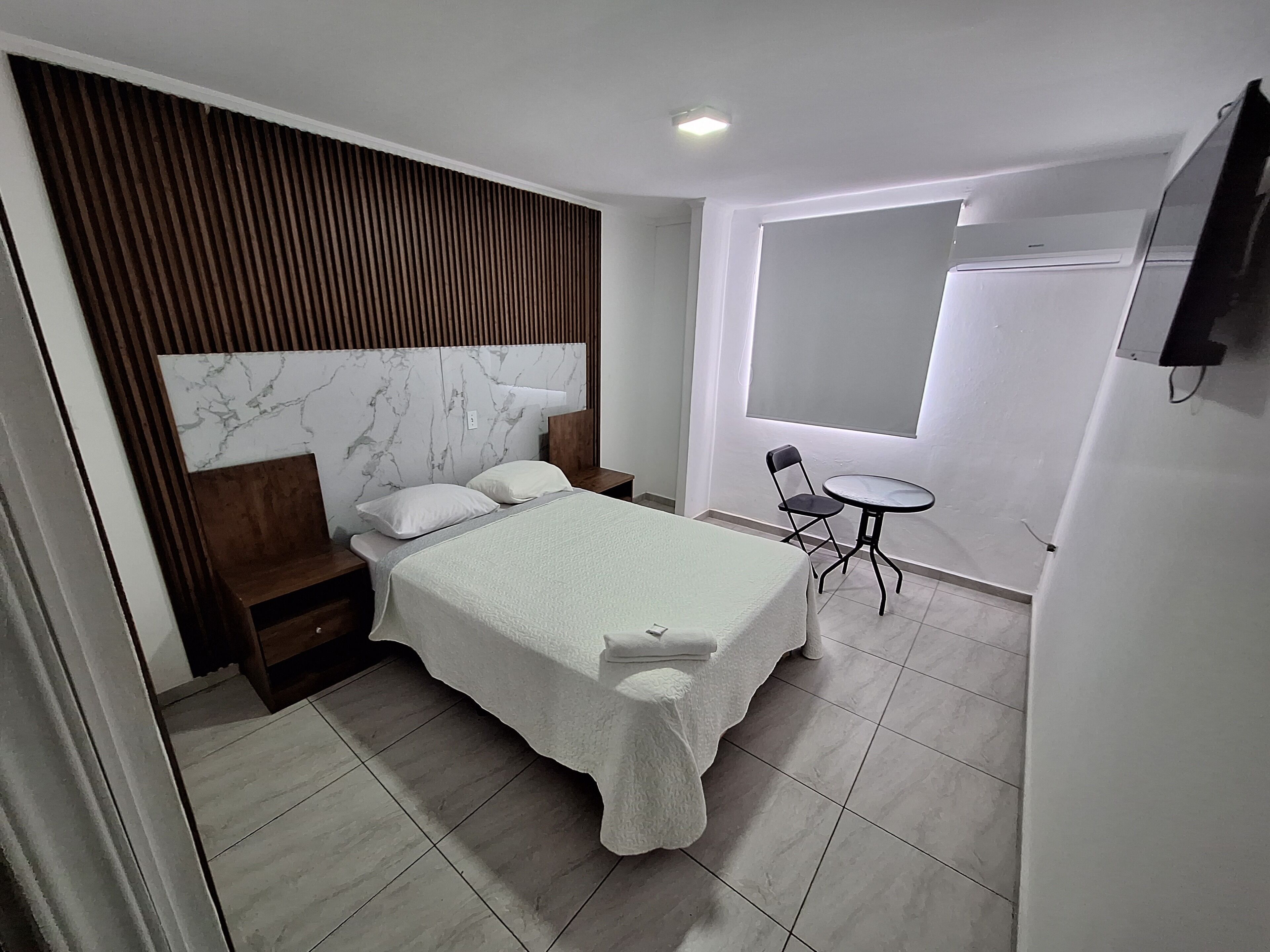 A bedroom with a bed, a small table, a chair, and a TV mounted on the wall.