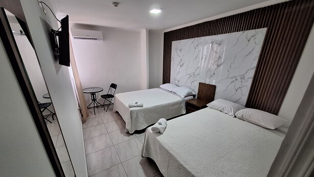 A hotel room with two single beds, a small table with a chair, a TV mounted on the wall, and a marble-patterned headboard. - Express Inn Panama International Airport Hostel (Tocumen)