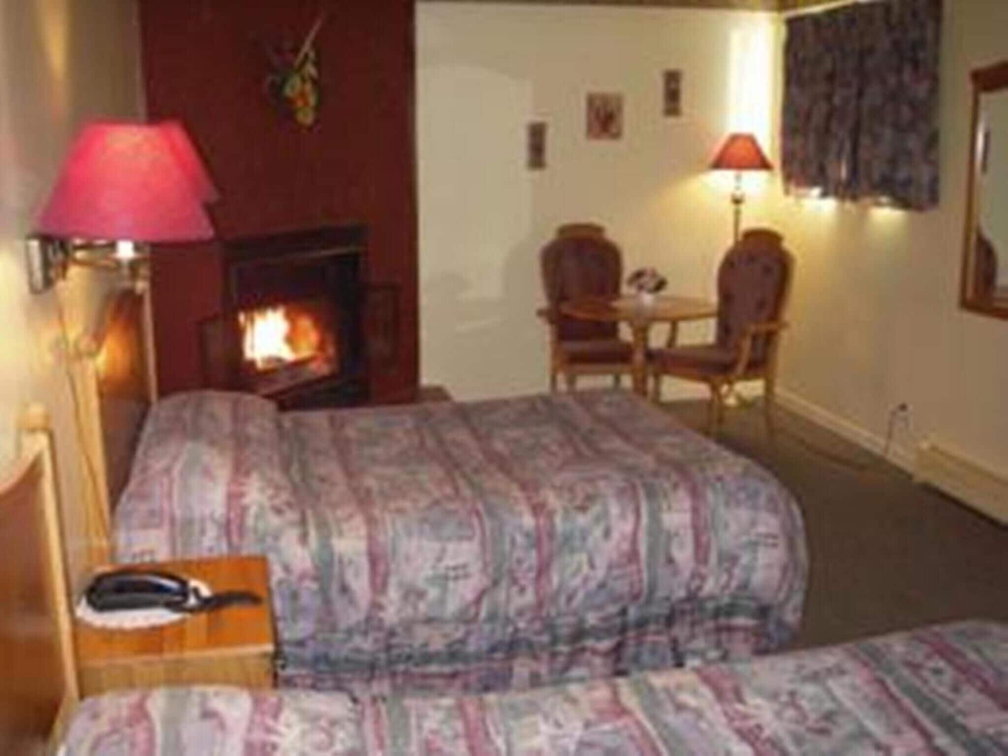A hotel room with two beds, a fireplace, a desk, and a chair.