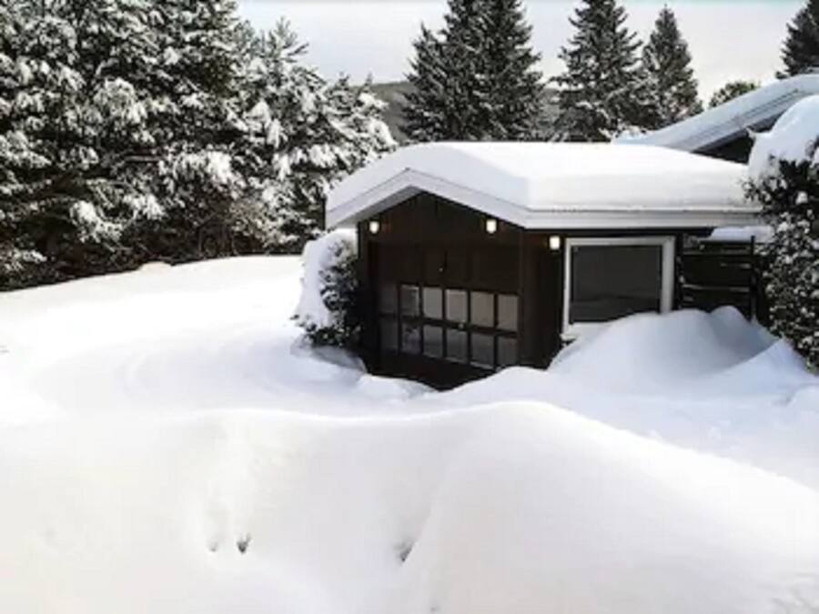 Une maison recouverte de neige, avec un garage et un petit porche.