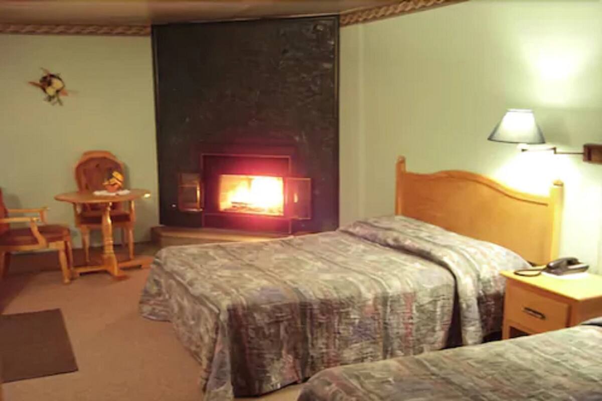 Une chambre d’hôtel avec deux lits, une petite table avec des chaises, une lampe et une cheminée.