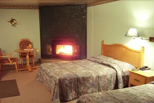 Une chambre d’hôtel avec deux lits, une petite table avec des chaises, une lampe et une cheminée.