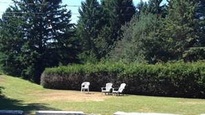 A paved area with three white chairs and a hedge in the background. - Auberge Mountain View Inn (Mont-Tremblant)