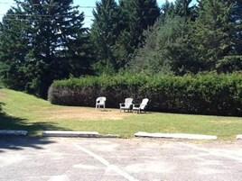 Une zone pavée avec trois chaises blanches et une haie en arrière-plan.