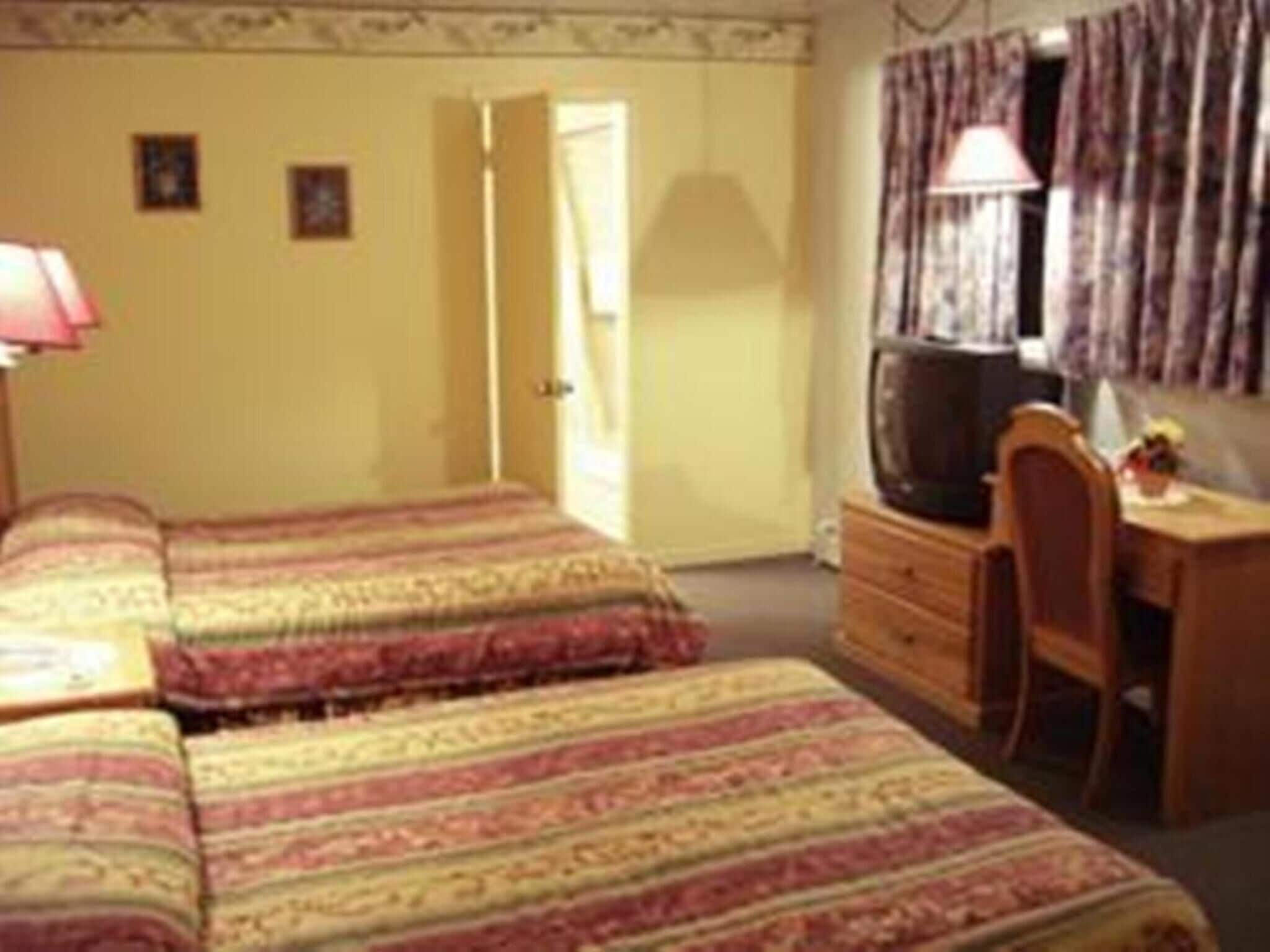 Une chambre avec deux lits, un bureau, une chaise, une télévision et une porte donnant sur une autre pièce.