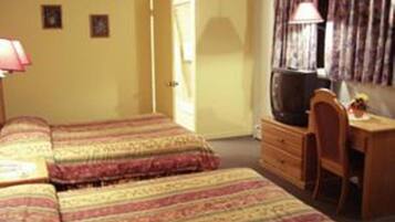 Une chambre avec deux lits, un bureau, une chaise, une télévision et une porte donnant sur une autre pièce.
