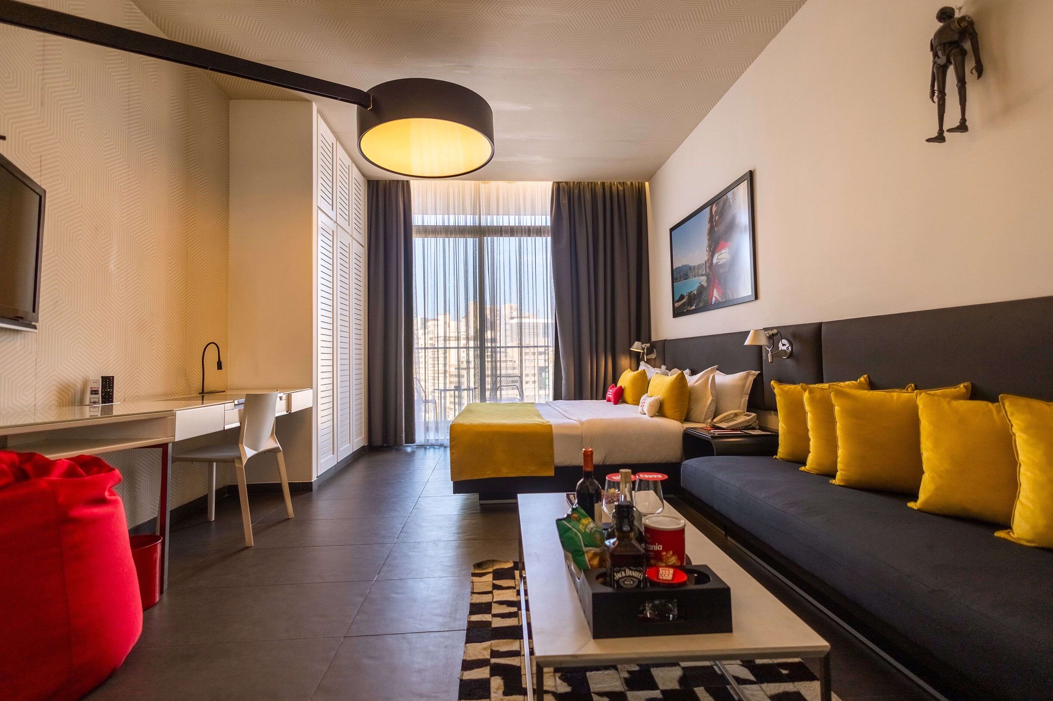 Una habitación de hotel moderna con cama, sofá, escritorio y un amplio ventanal.
