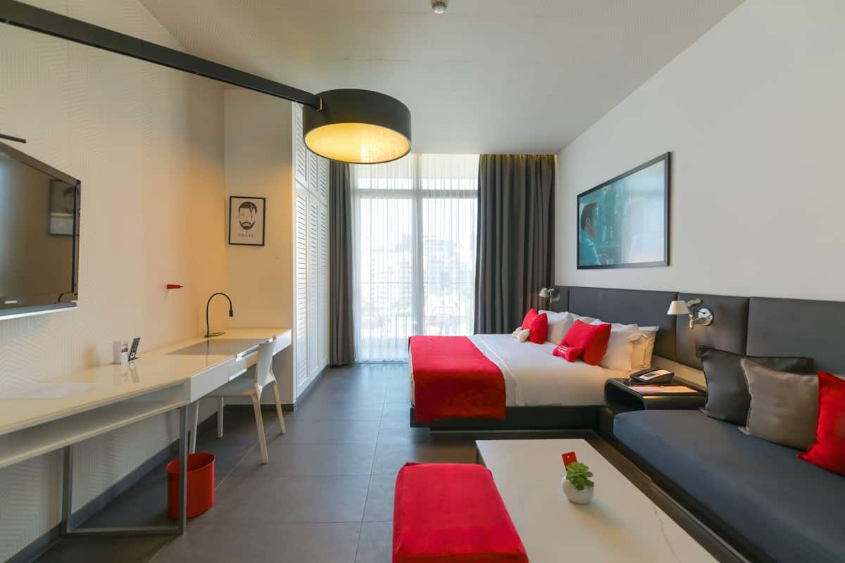 A hotel room with a desk, two beds, a sofa, a coffee table, a TV, and a large window.