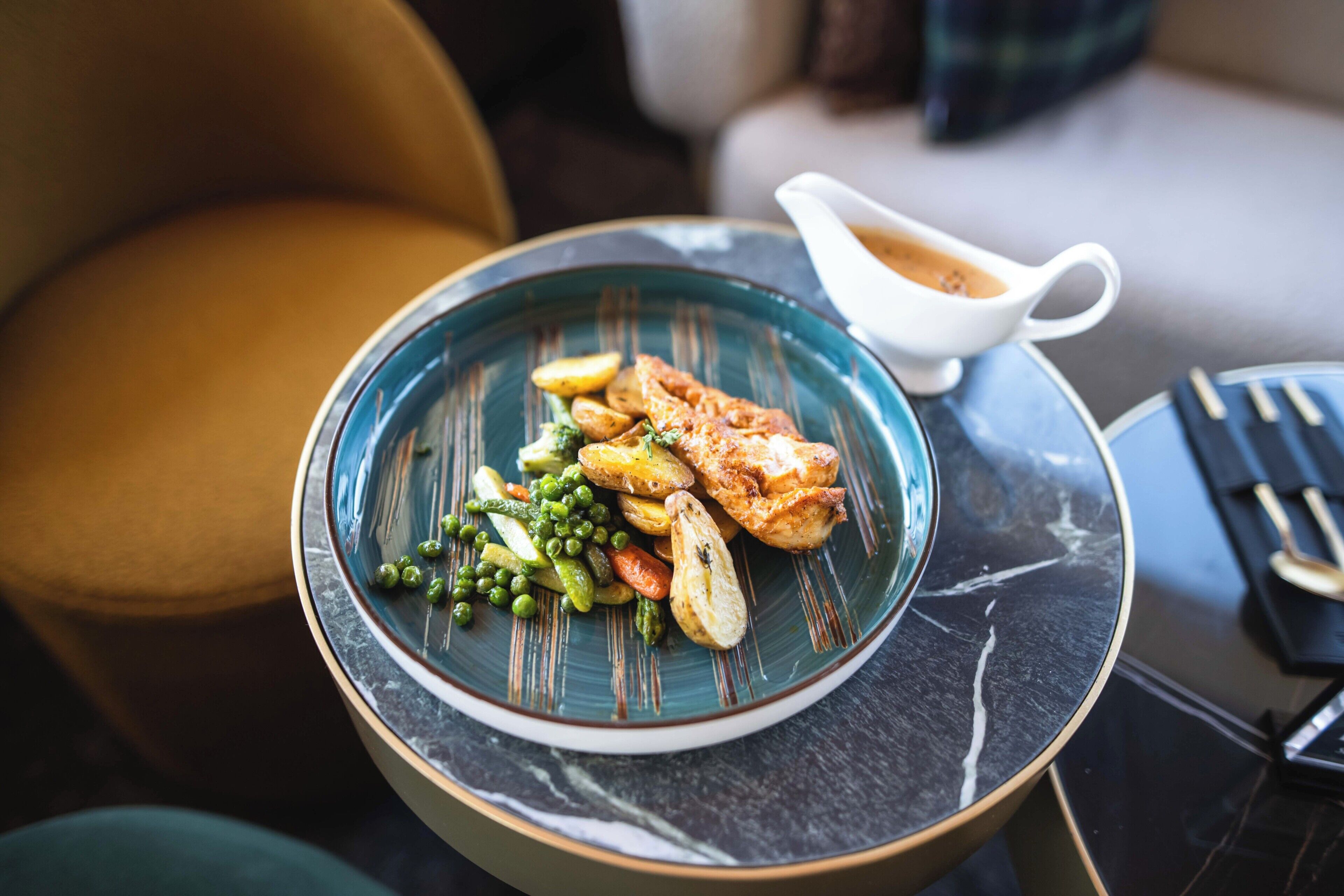 A plate of food with peas, carrots, and potatoes, and a gravy boat on a table.