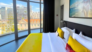A hotel room with a large bed, a city view, and a geometric ceiling pattern. - The Smallville Hotel (Beirut)