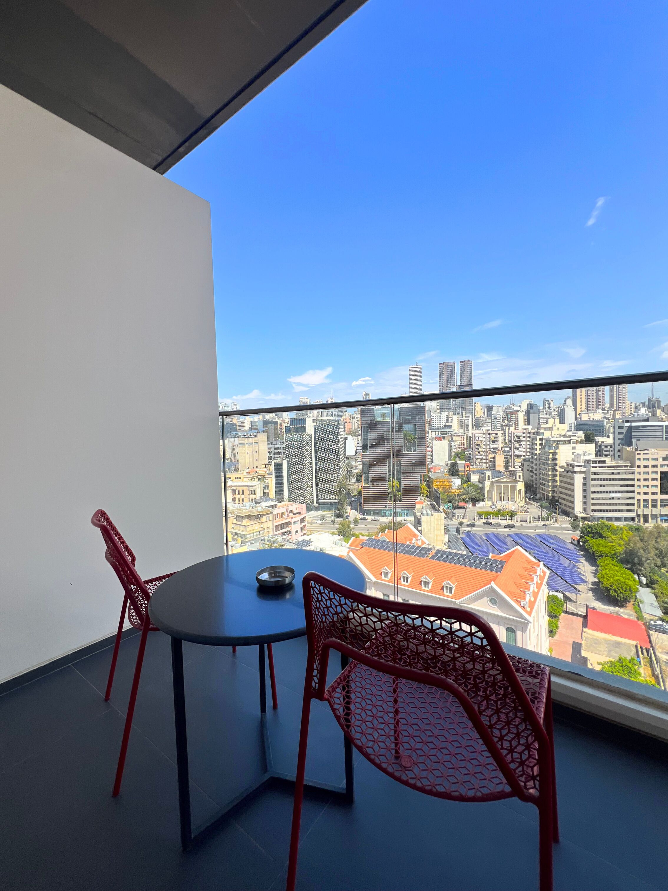 Un balcón con mesa y sillas, con vista a un paisaje urbano con edificios y paneles solares.