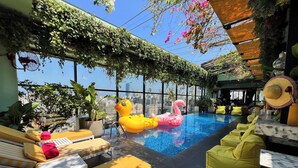 An indoor swimming pool with lounge chairs, a city view, and greenery. - The Smallville Hotel (Beirut)