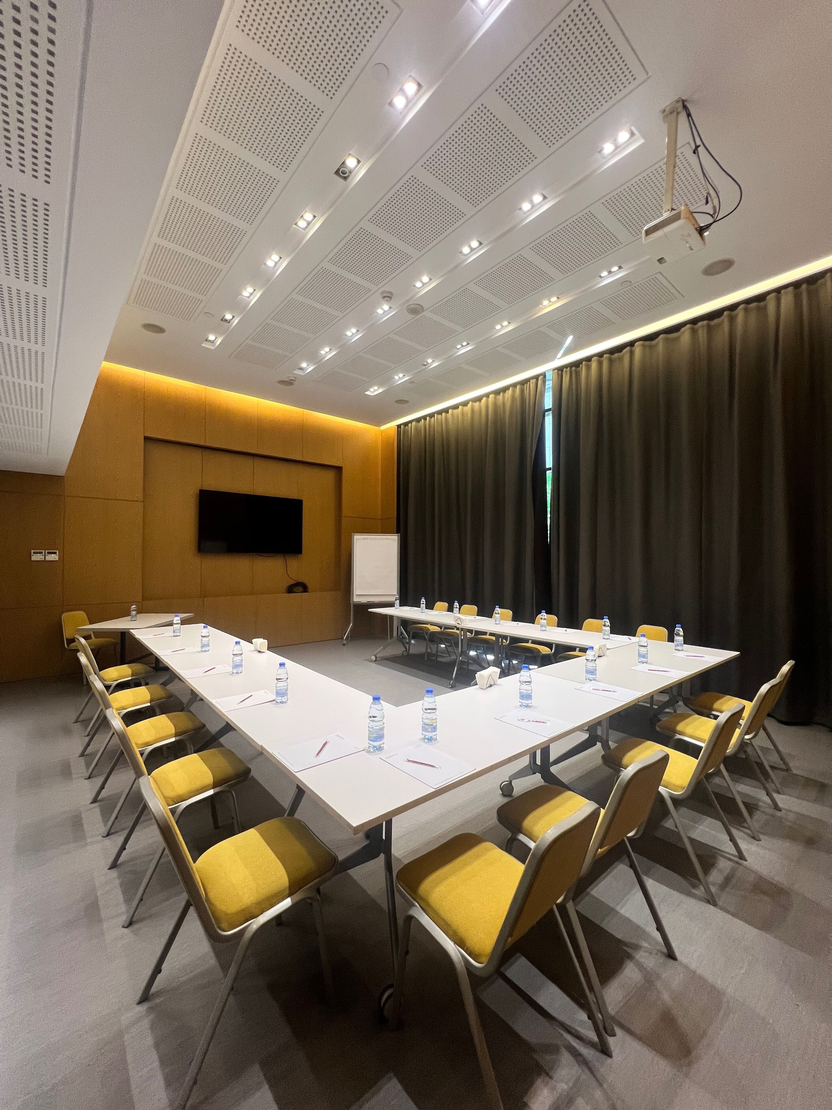 A conference room with a long table, yellow chairs, a whiteboard, and a projector.