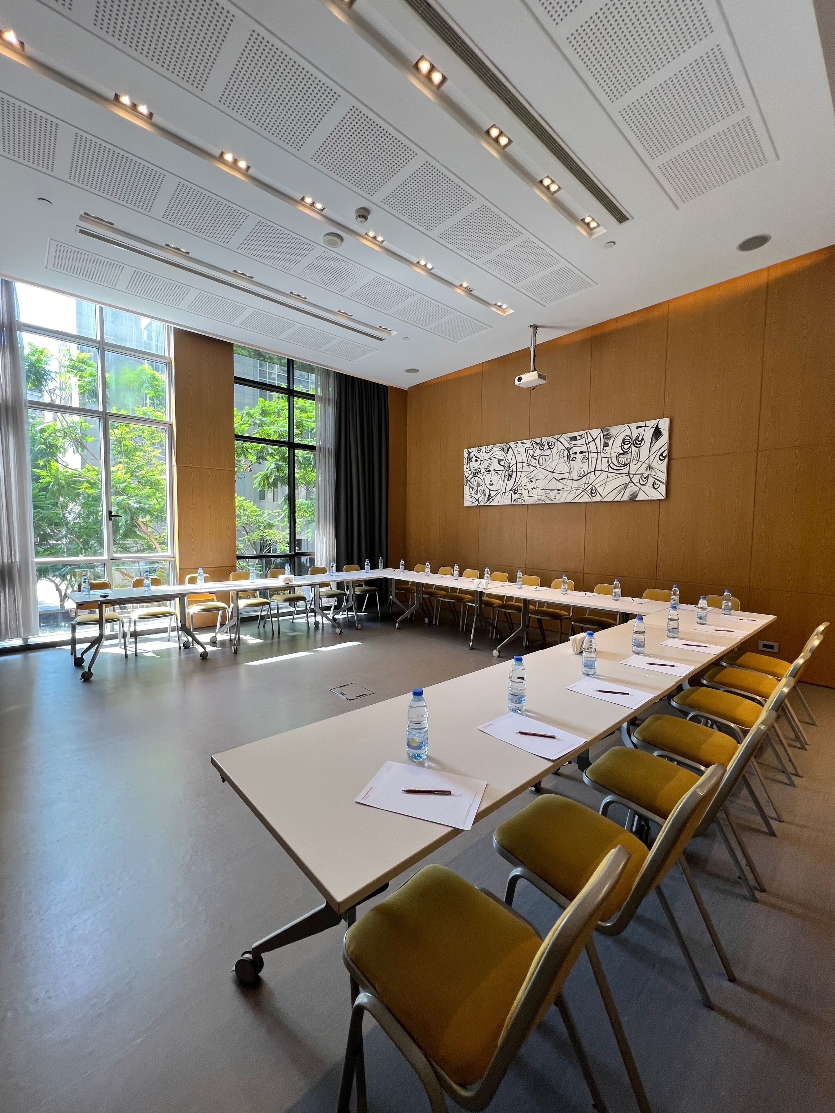 A conference room with a long table, yellow chairs, water bottles, and a projector on the wall.