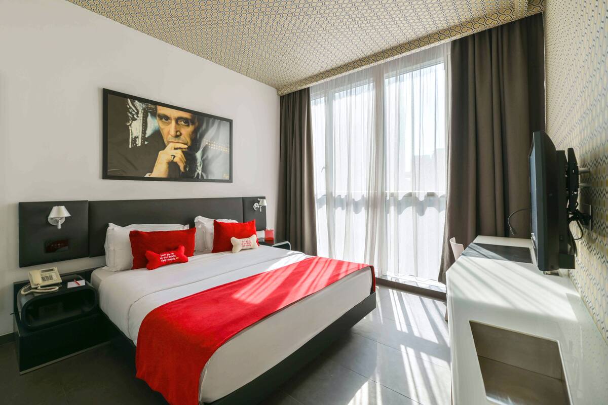 A hotel room with a large bed, a desk, a TV, and a painting on the wall.