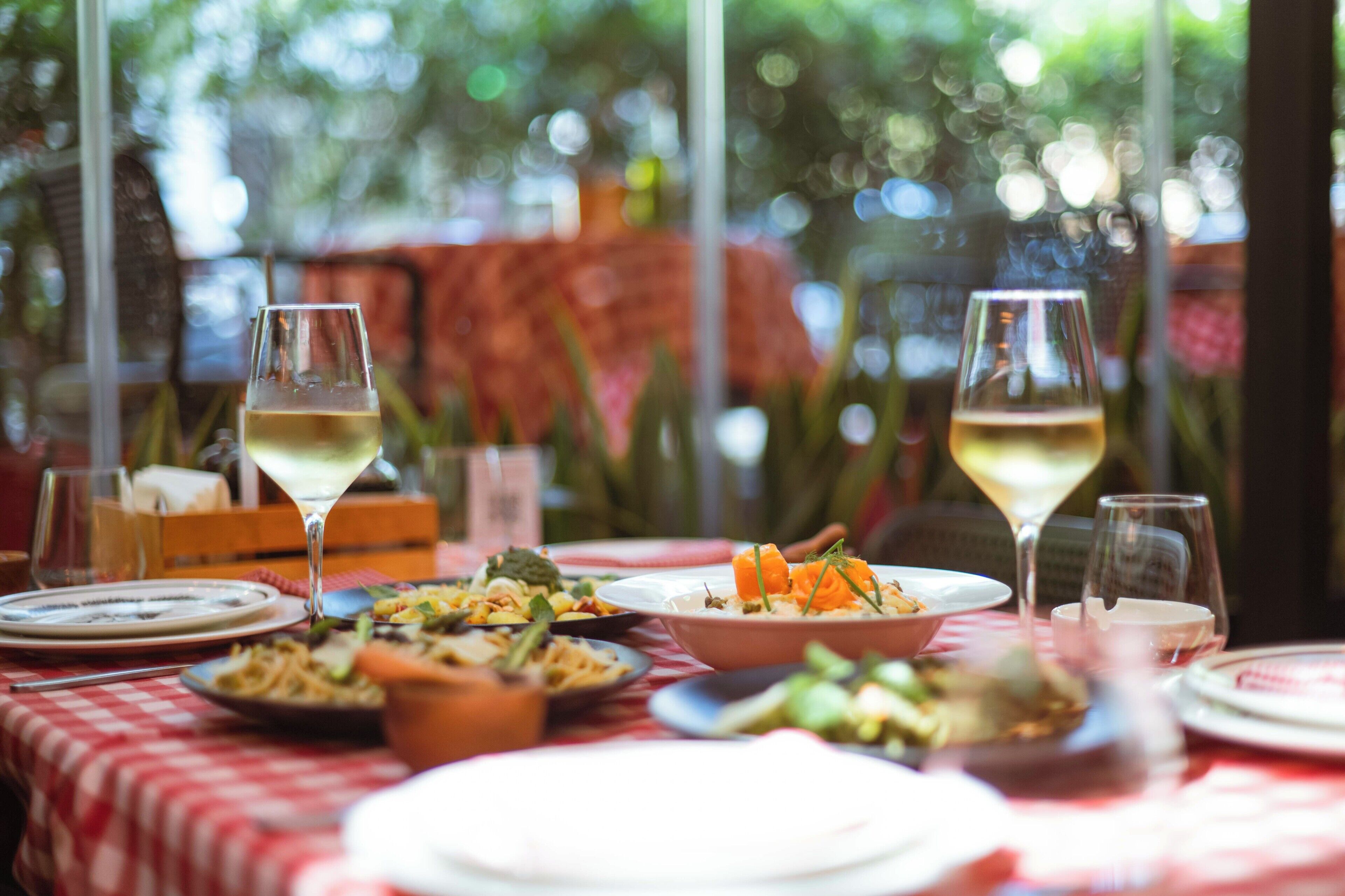 A dining table with various dishes and glasses of wine, set against a red and white checkered tablecloth.