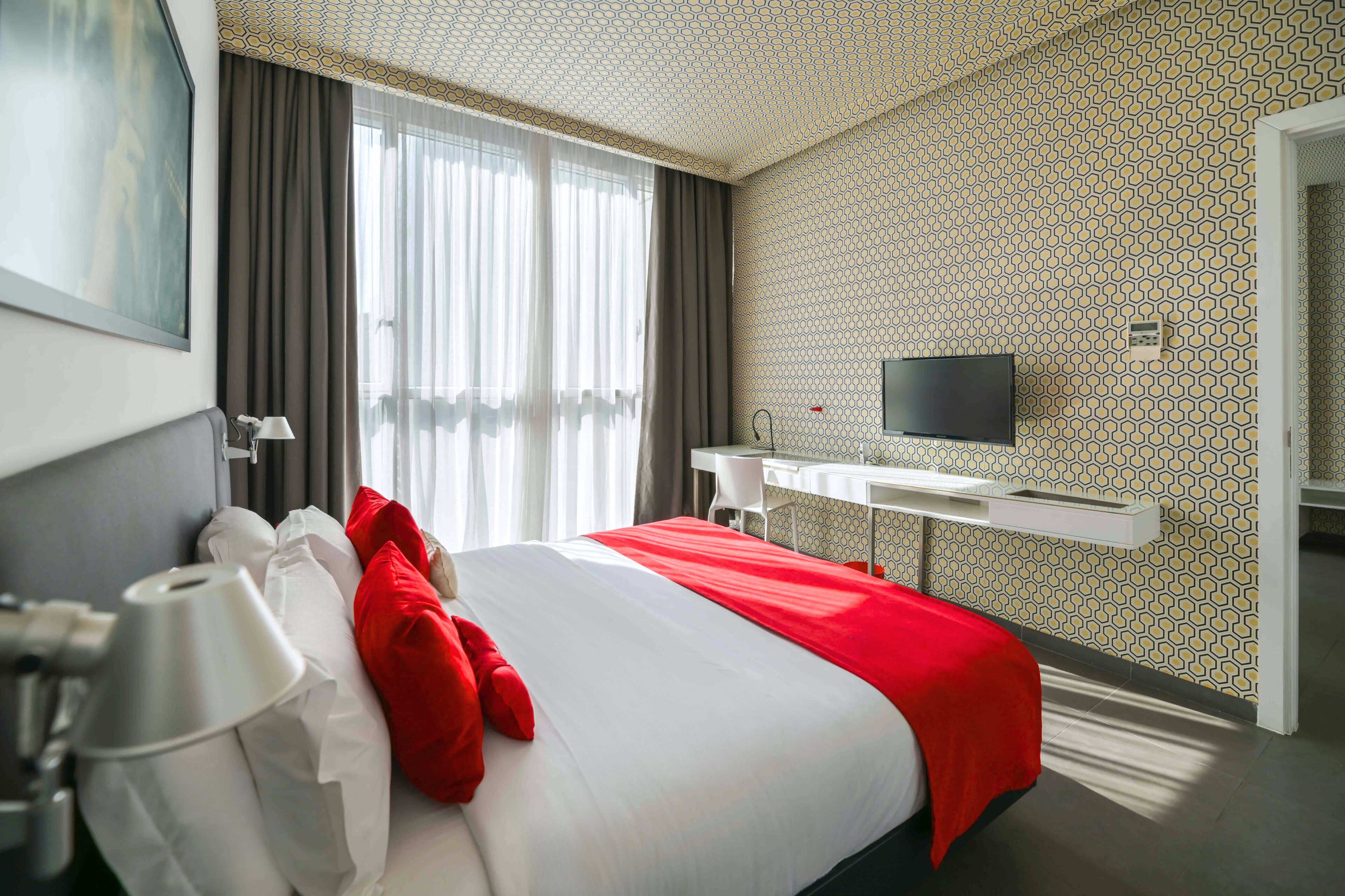 Quarto de hotel com cama grande, escrivaninha, TV de tela plana e banheiro visível por uma porta aberta.