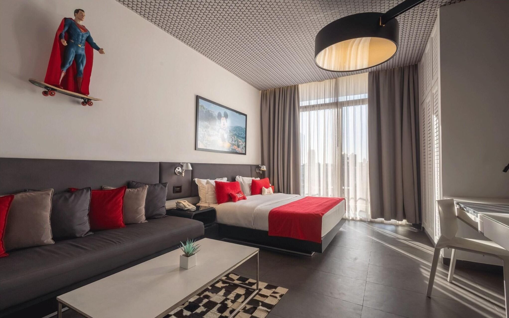 A modern hotel room with a sofa, a bed, a desk, and a large window.