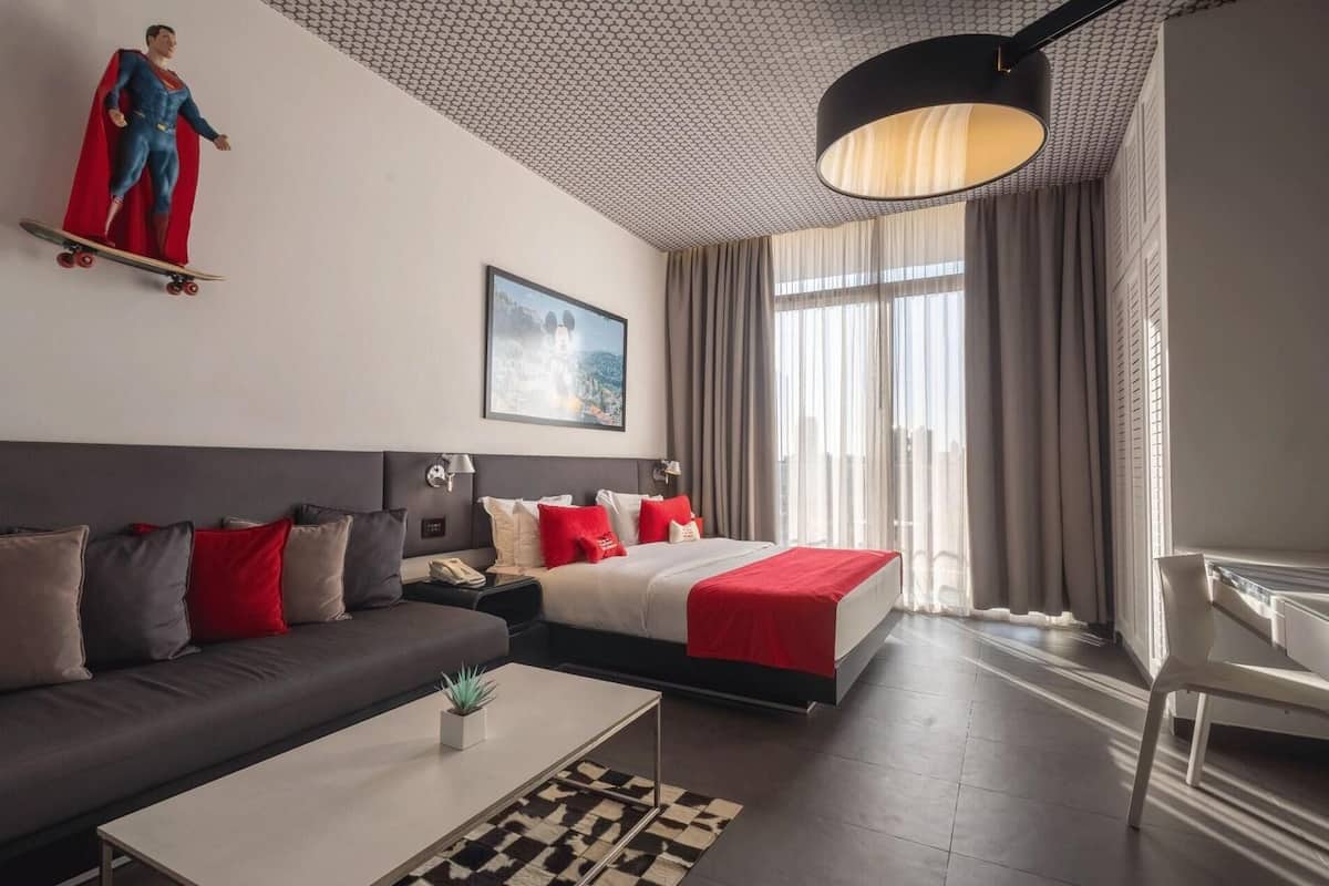 A modern hotel room with a sofa, a bed, a desk, and a large window.