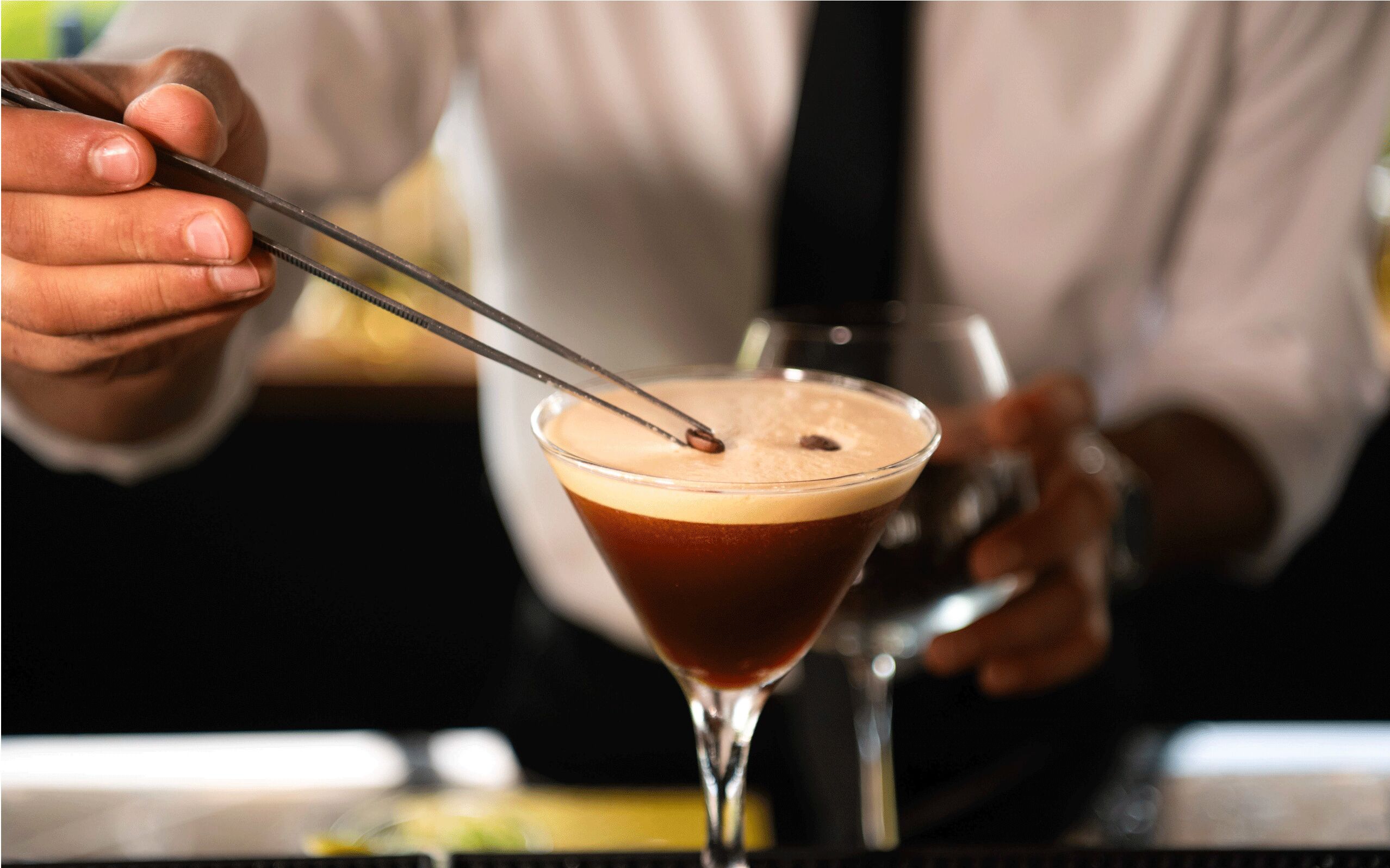 A person using chopsticks to stir a cocktail in a martini glass.