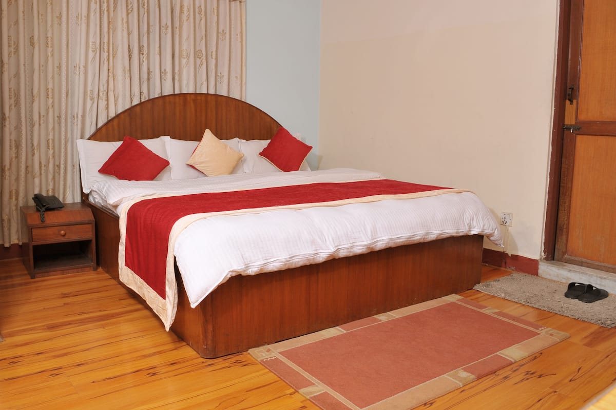 A neatly made bed with a wooden headboard, a nightstand with a lamp, and a pair of shoes on the floor.