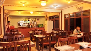 A restaurant interior with wooden tables and chairs, a bar area with bottles, and a clock on the wall. - Hotel Brihaspati (Kathmandu)