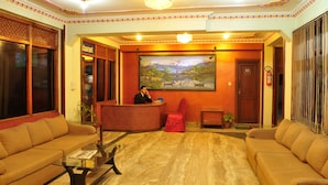 A reception area with a receptionist, a reception desk, two sofas, a coffee table, a painting, and a fire extinguisher. - Hotel Brihaspati (Kathmandu)