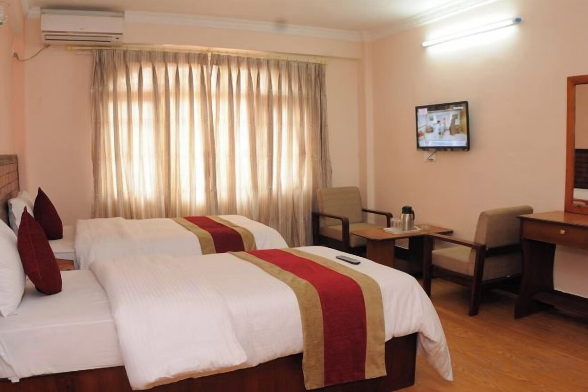 Ein Hotelzimmer mit zwei Betten, einem Schreibtisch, einem Stuhl und einem an der Wand befestigten Fernseher.