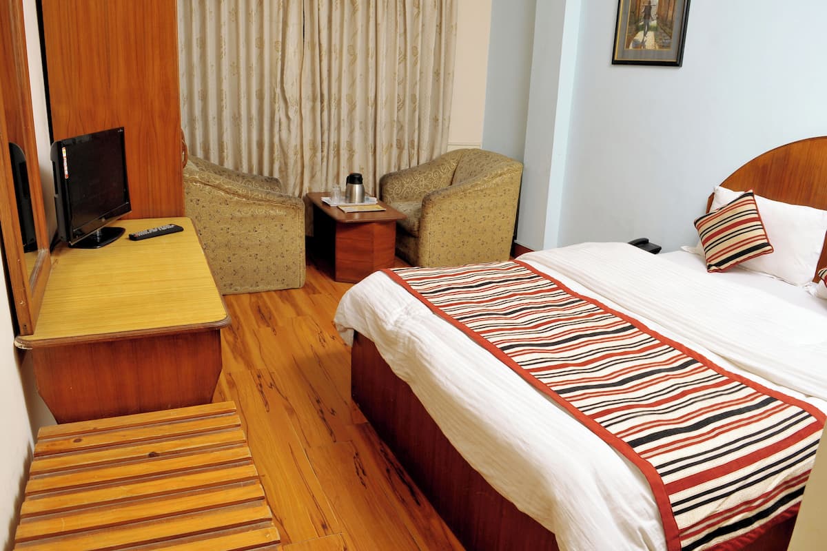 A hotel room with a bed, a desk, a chair, a small table, and a television.
