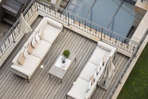 Una terraza en la azotea con piso de madera, mobiliario exterior blanco y una mesa pequeña con una planta.
