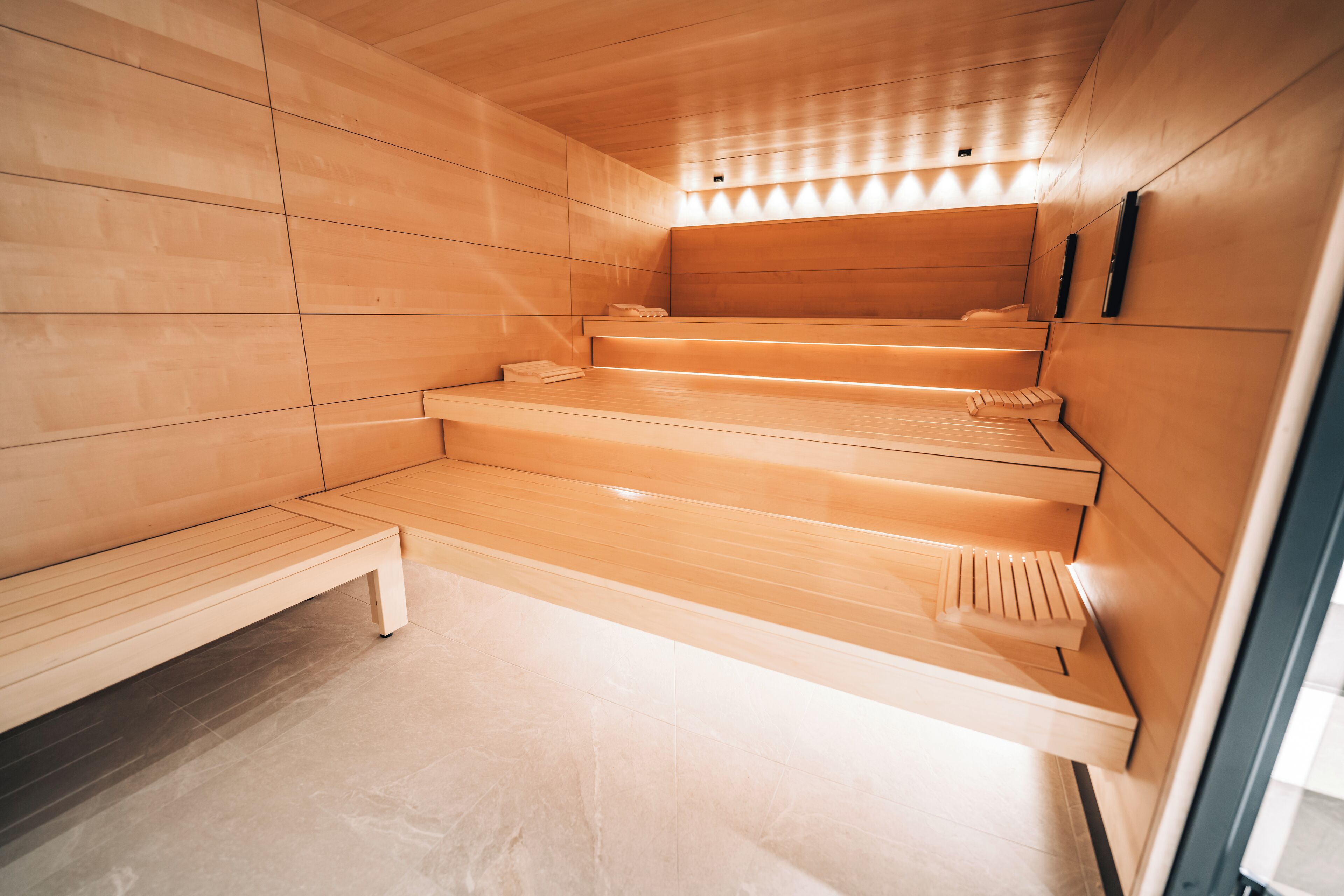 Una sauna con panche e gradini in legno, una panca a sinistra e un riscaldatore a parete a destra.