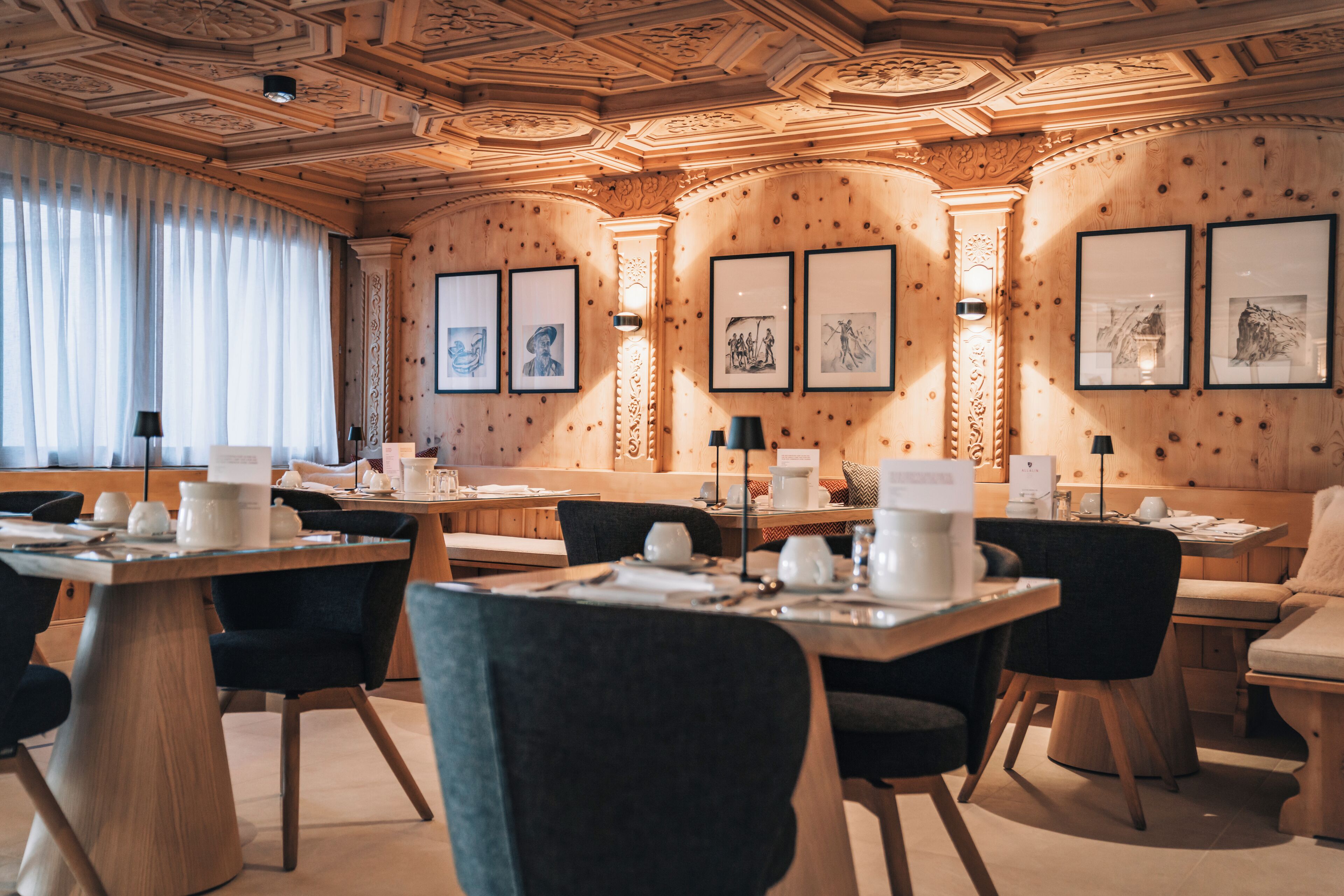 A hotel dining area with wooden panel walls, framed artwork, and a mix of seating options including tables and benches.