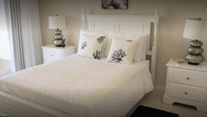 Un dormitorio ordenado con una cama grande, dos mesitas de noche con lámparas y una ventana que proporciona luz natural.