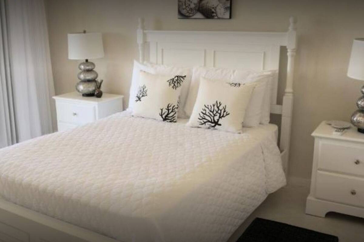 Un dormitorio ordenado con una cama grande, dos mesitas de noche con lámparas y una ventana que proporciona luz natural.