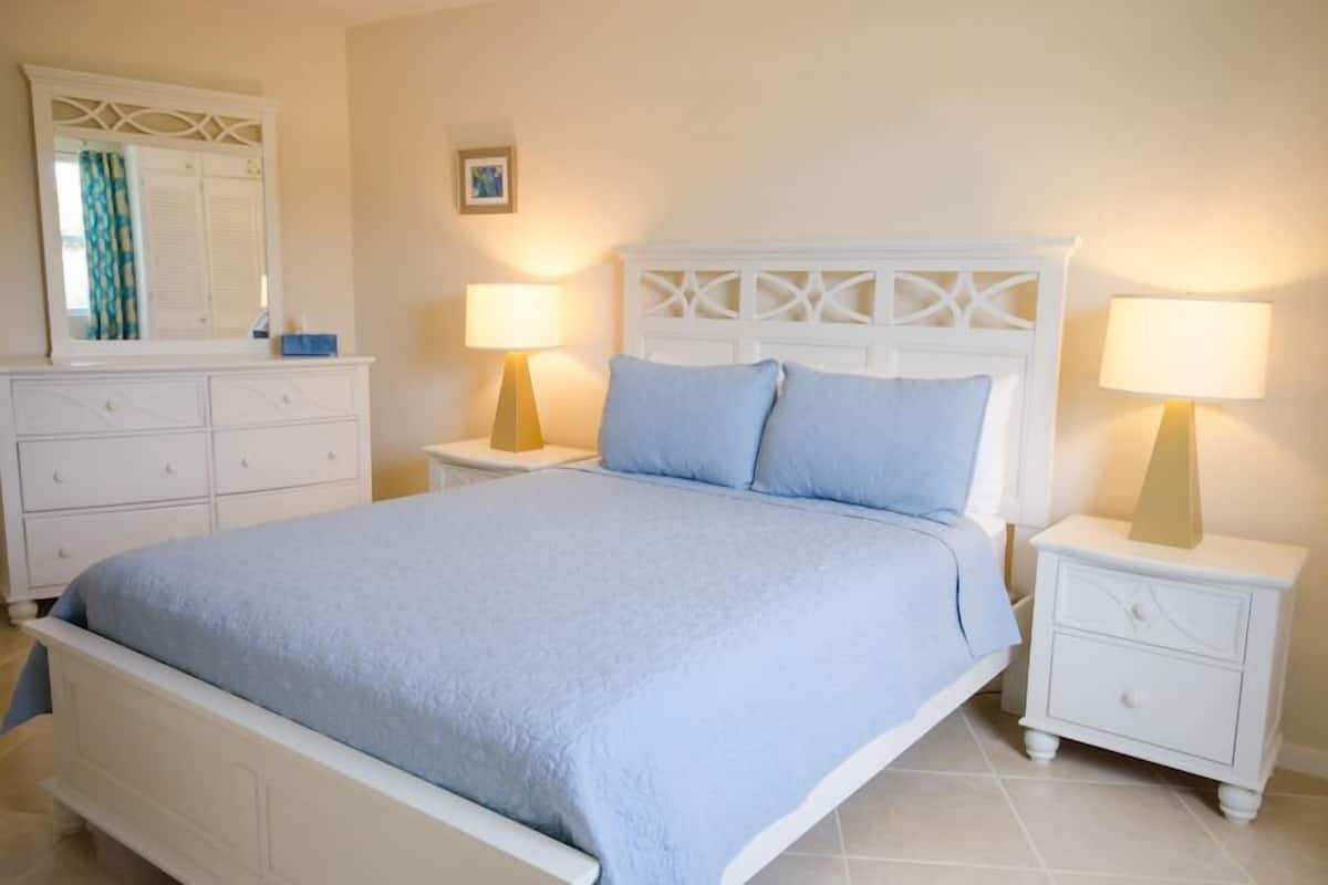 Un dormitorio con cama, mesitas de noche blancas, cómoda y espejo.