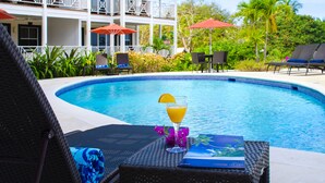 Zona de piscina con sillones de descanso, una bebida y un libro sobre una mesa.